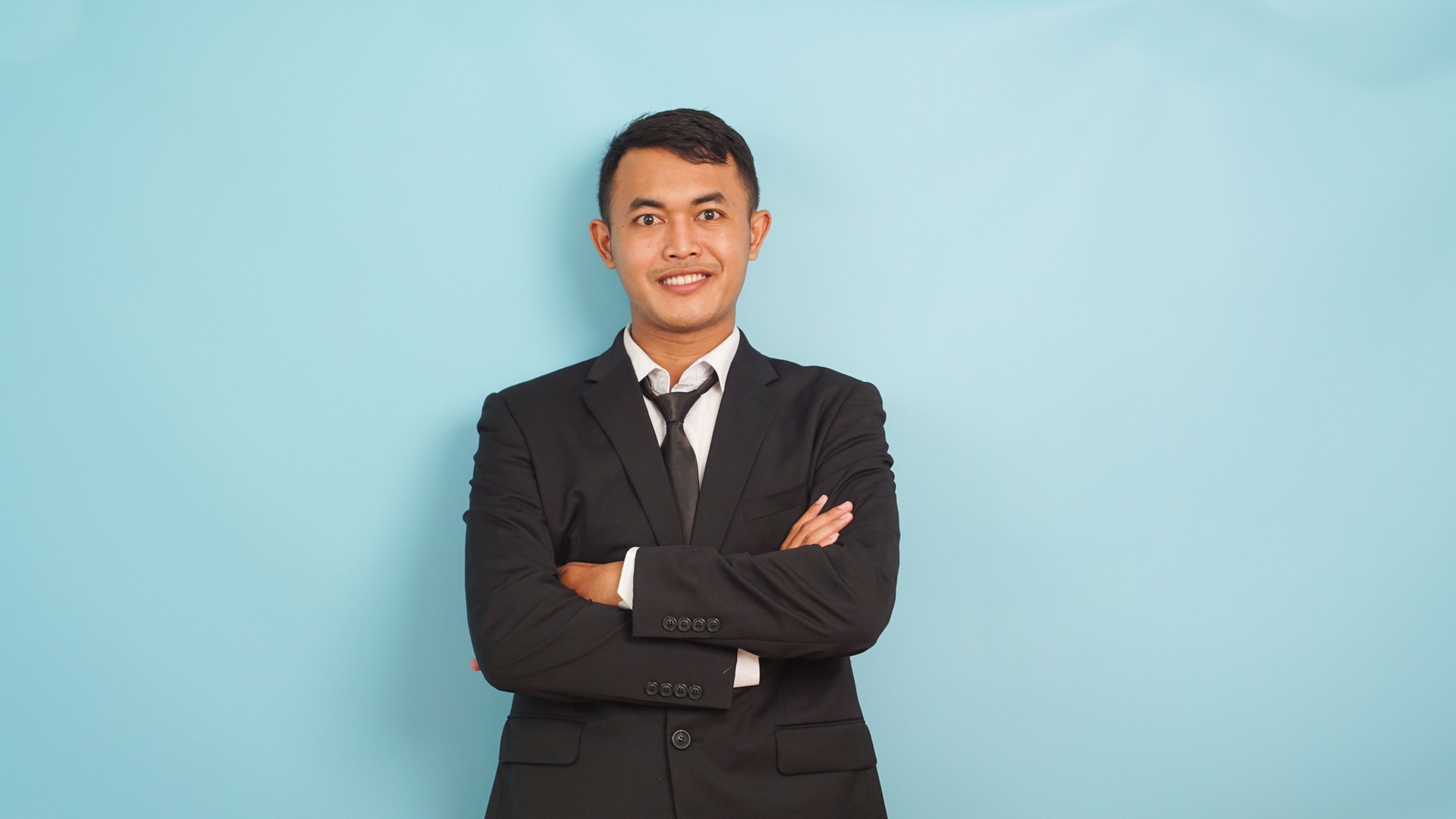 Portrait young Asian businessman happy and smiling, look at camera, crossed arm, light blue background